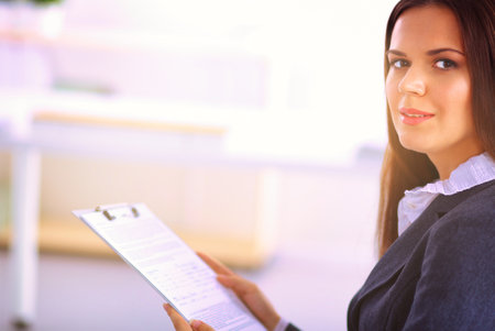 Attractive young businesswoman standing near desk with folder in the officeの写真素材