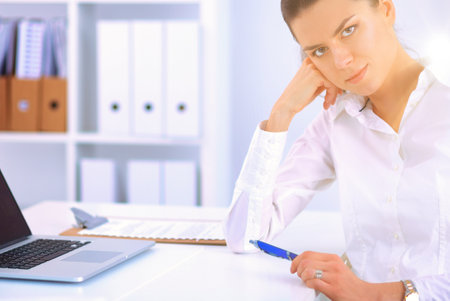 Attractive businesswoman sitting on a desk with laptop in the officeの写真素材