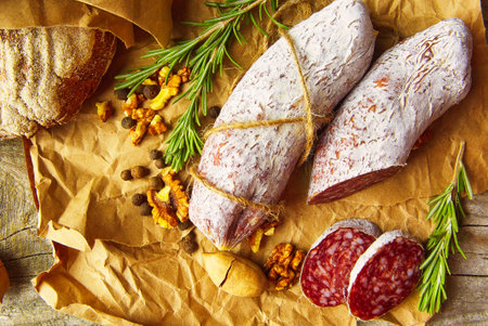 Italian salami wih sea salt, rosemary, garlic and nuts on paper. Rustic style. Top view.の写真素材