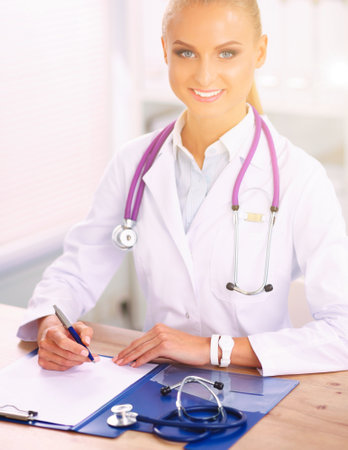 Beautiful young smiling female doctor sitting at the desk and writing.の写真素材
