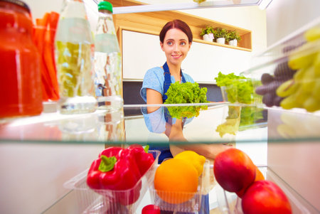 Portrait of female standing near open fridge full of healthy food, vegetables and fruits. Portrait of femaleの写真素材