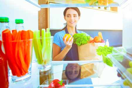 Portrait of female standing near open fridge full of healthy food, vegetables and fruits. Portrait of femaleの写真素材