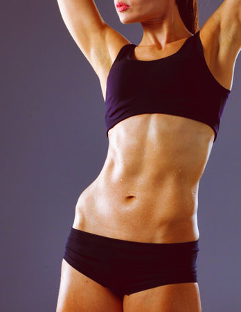 Muscular young woman standing on gray background. Muscular young womanの写真素材
