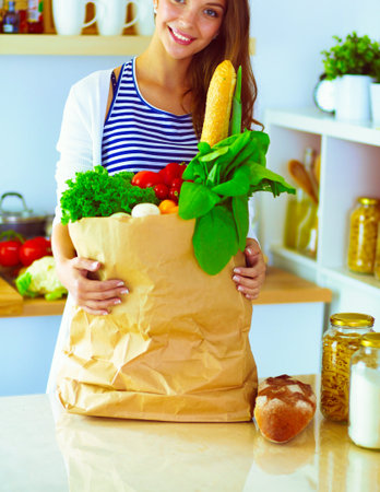 Young woman holding grocery shopping bag with vegetables .Standing in the kitchen.の写真素材