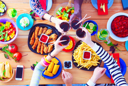 Top view of group of people having dinner together while sitting at wooden table. Food on the table. People eat fast food.の写真素材