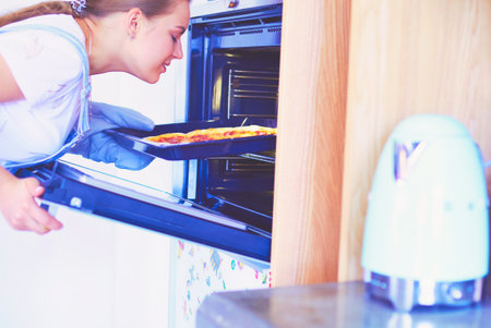 Happy young woman cooking pizza at homeの写真素材
