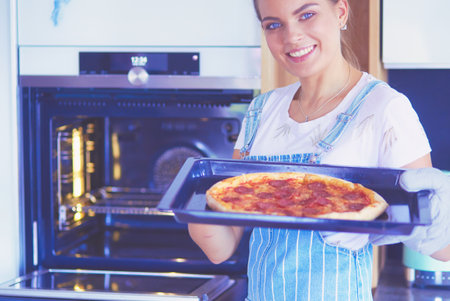 Happy young woman cooking pizza at homeの写真素材