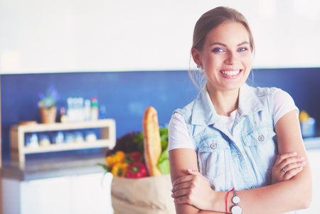 Portrait of young woman standing with arms crossed against kitchen backgroundの写真素材