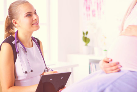 Young woman doctor with stethoscope and tablet speaking with pregnant woman at hospital.の写真素材