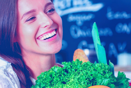 Smiling young woman holding vegetables standing in kitchen. Smiling young womanの写真素材