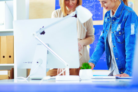 Two young woman standing near desk with instruments, plan and laptop.の写真素材