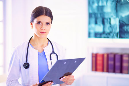 Young smiling female doctor with stethoscope holding a folder at doctors officeの写真素材