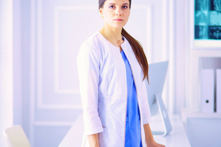 Portrait of young woman doctor in white coat standing in hospitalの写真素材