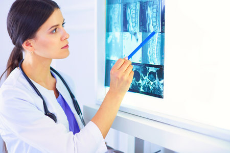 Young smiling female doctor with stethoscope pointing at X-ray at doctors officeの写真素材