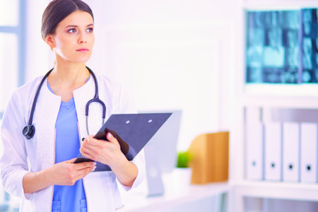 Young smiling female doctor with stethoscope holding a folder at a hospitals consulting roomの写真素材