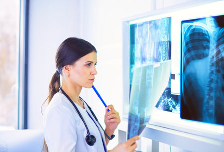 Young female doctor with stethoscope examining X-ray at doctors officeの写真素材