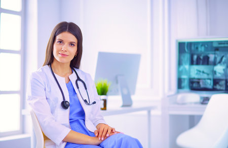 Beautiful female doctor sitting in a consulting room, smiling at the cameraの写真素材