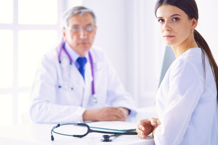 A doctor looking at the camera with her male colleage in the back of the conference room in hospitalの写真素材