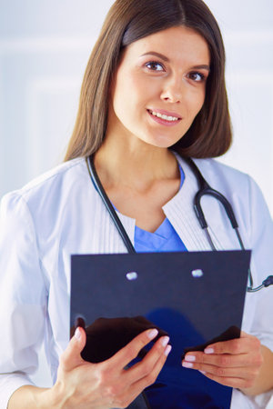 Female doctor standing with a folder in her hands at hospital, smiling at the cameraの写真素材