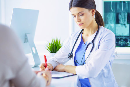 Doctor and patient discussing medical problems in a hospital consulting room. Doc filling in a patients formの写真素材