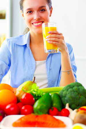 Young and cute woman sitting at the table full of fruits and vegetables in the wooden interiorの写真素材
