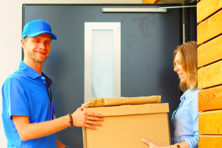 Smiling delivery man in blue uniform delivering parcel box to recipient - courier service concept. Smiling delivery man in blue uniformの写真素材
