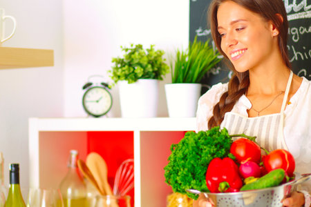 Smiling young woman holding vegetables standing in kitchen. Smiling young womanの写真素材