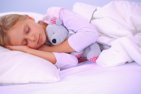 Child little girl sleeps in the bed with a toy teddy bear.の写真素材