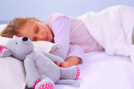 Child little girl sleeps in the bed with a toy teddy bear.の写真素材