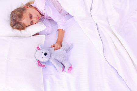 Child little girl sleeps in the bed with a toy teddy bear.の写真素材