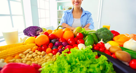 Young and cute woman sitting at the table full of fruits and vegetables in the wooden interiorの写真素材