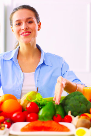 Young and cute woman sitting at the table full of fruits and vegetables in the wooden interiorの写真素材