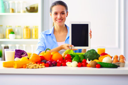 Young and cute woman sitting at the table full of fruits and vegetables in the wooden interiorの写真素材