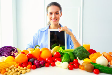 Young and cute woman sitting at the table full of fruits and vegetables in the wooden interior, holding tabletの写真素材