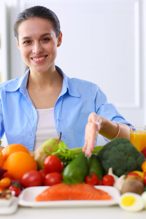 Young and cute woman sitting at the table full of fruits and vegetables in the wooden interiorの写真素材