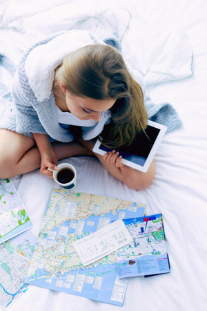 Relaxed young woman sitting on bed with a cup of coffee and digital tabletの写真素材