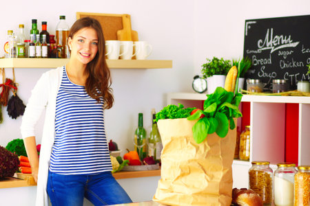 Young woman holding grocery shopping bag with vegetables .Standing in the kitchen. Young womanの写真素材