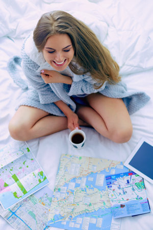 Relaxed young woman sitting on bed with a cup of coffee and digital tabletの写真素材