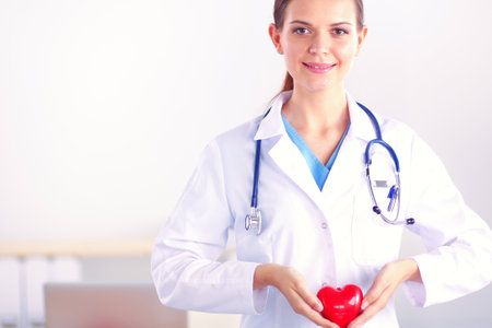 Beautiful young smiling female doctor sitting at the desk and holding heart.の写真素材
