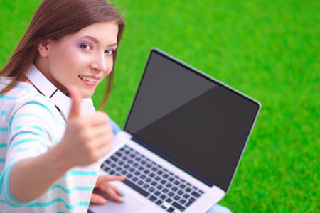 Young woman with laptop sitting on green grassの写真素材
