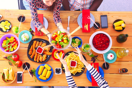Top view of group of people having dinner together while sitting at wooden table. Food on the table. People eat fast food.の写真素材