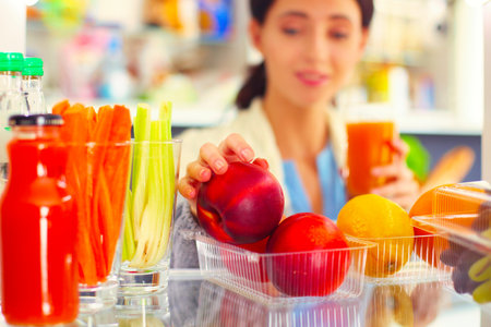 Portrait of female standing near open fridge full of healthy food, vegetables and fruits. Portrait of femaleの写真素材