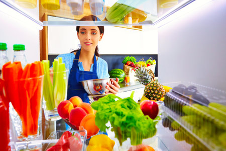 Portrait of female standing near open fridge full of healthy food, vegetables and fruits. Portrait of femaleの写真素材