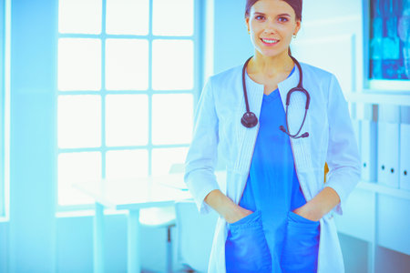 Female doctor standing with stethoscope and her hands in pockets at hospitalの写真素材