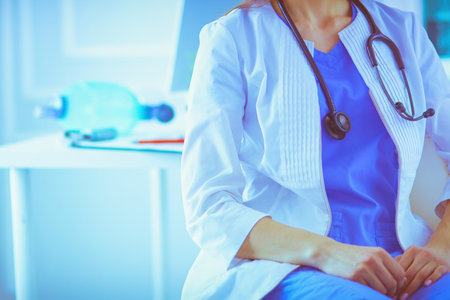 Beautiful female doctor sitting at her working place in a consulting room, smiling at the cameraの写真素材