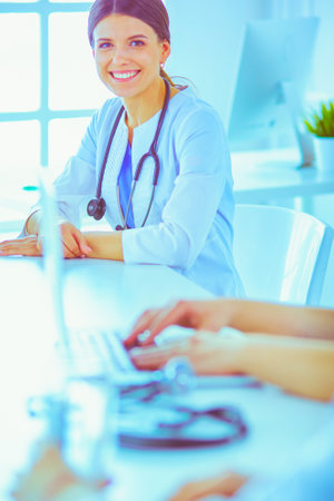 Smiling doctor using a laptop working with her colleagues in a bright hospital roomの写真素材