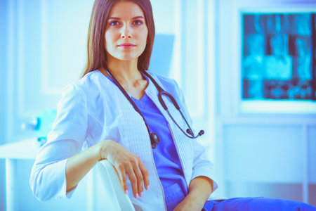 Beautiful female doctor sitting at her working place in a consulting room, smiling at the cameraの写真素材