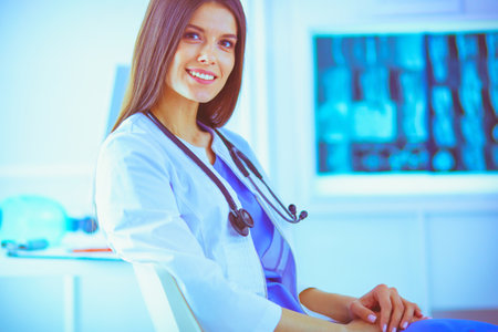 Beautiful female doctor sitting in a consulting room, smiling at the cameraの写真素材