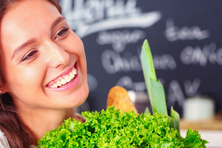 Smiling young woman holding vegetables standing in kitchen. Smiling young womanの写真素材