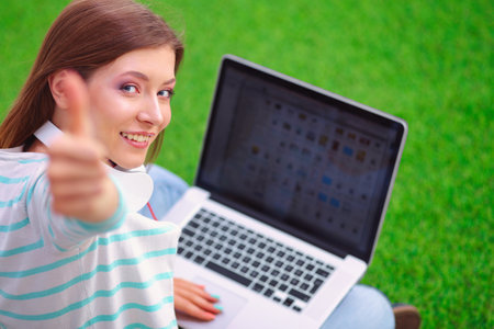 Young woman with laptop sitting on green grass . Portreit young womanの写真素材